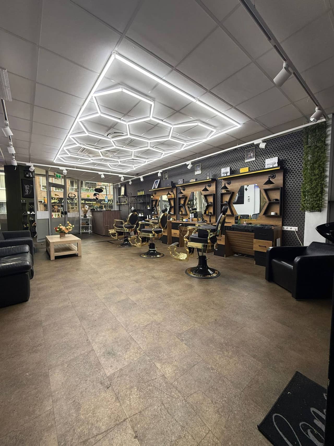 De zaak van binnen: gouden kappersstoelen op een rij, spiegels aan de wand en een zithoek bij het raam.
